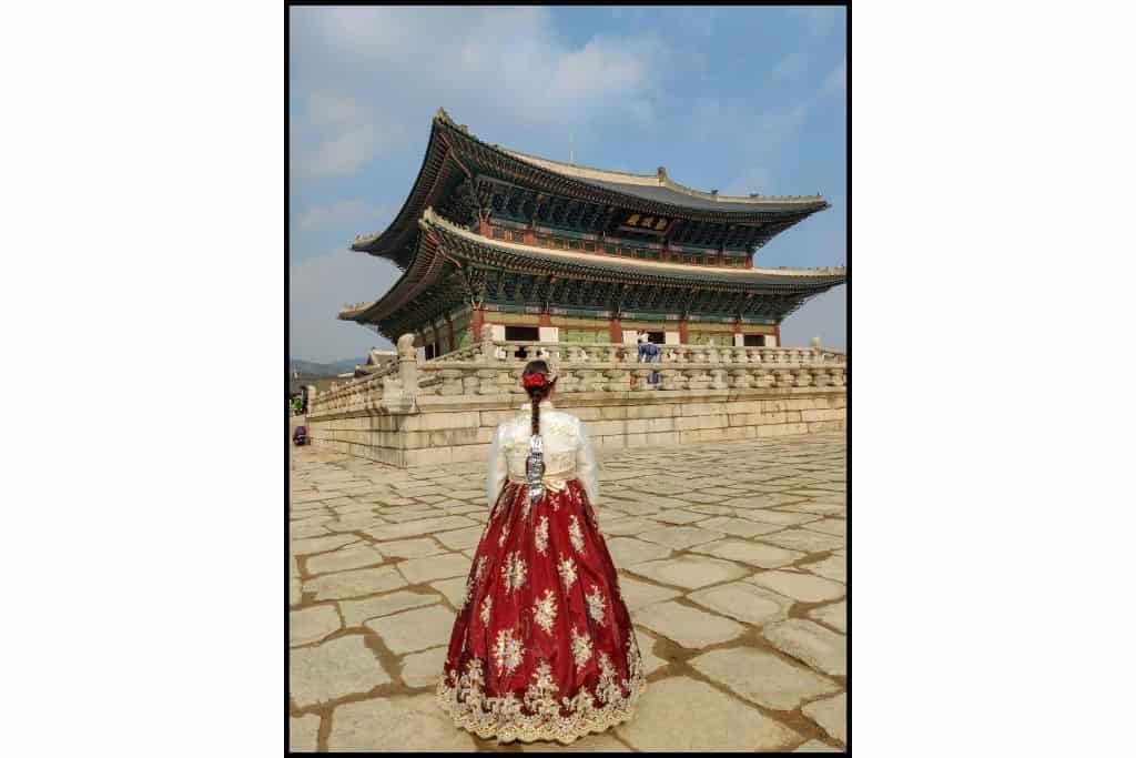 A woman wearing a traditional hanbok in front of a palace.