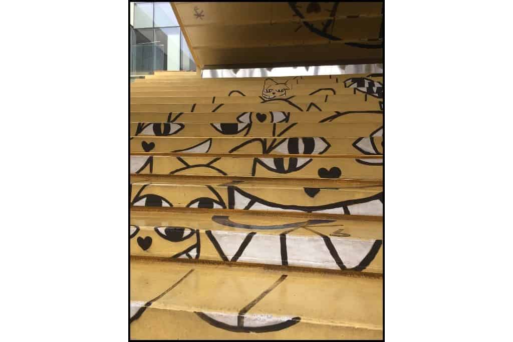Stairs painted primarily yellow with grinning cat faces. 