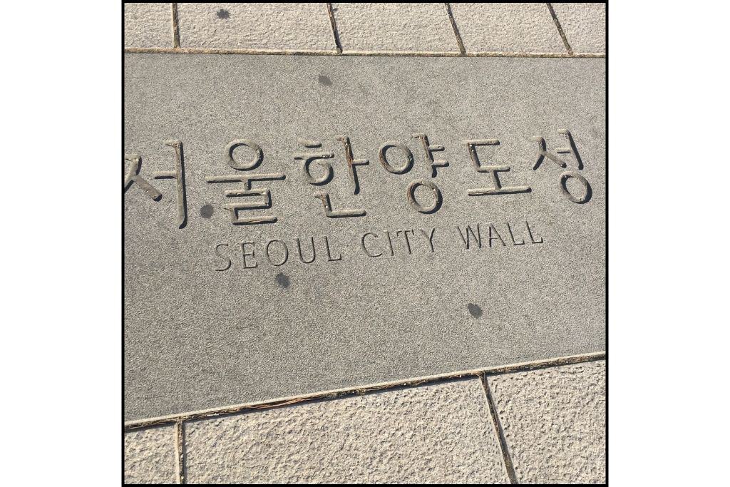 A sign for Seoul City Wall in the sidewalk engraved in Hangul and English