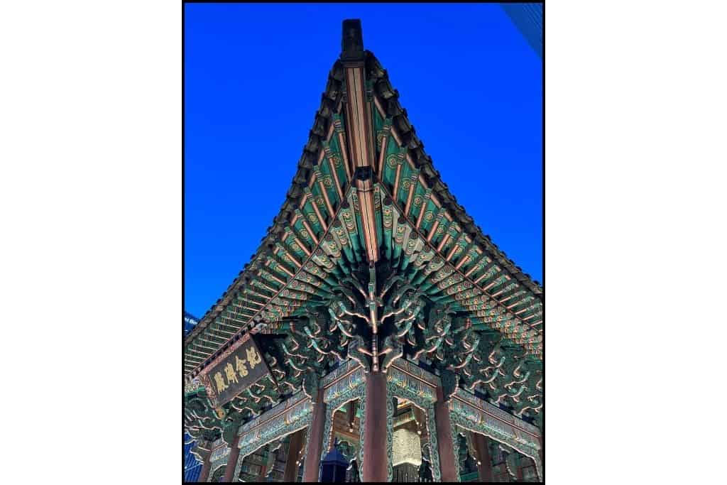 The corner of a Korean temple at night with a glowing blue sky behind it 