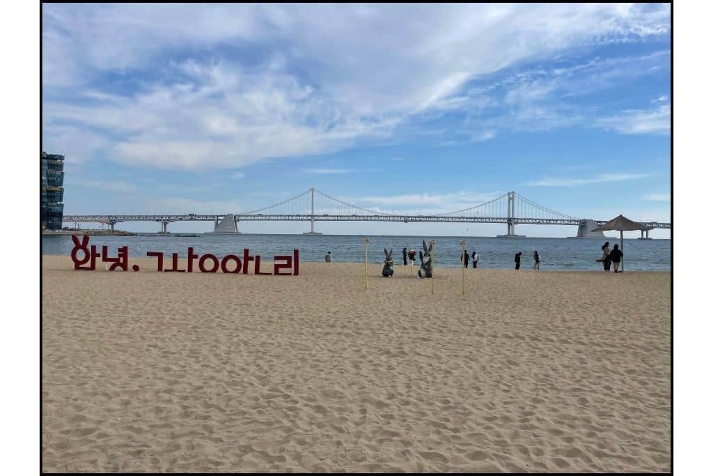 A sign for Gwangalli Beach in Hangul on the beach with the famous Diamond Bridge