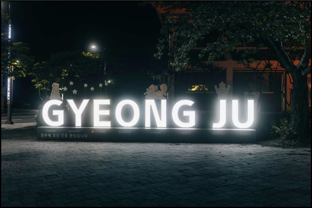 A brightly lit Gyeongju sign at night, with colorful lights illuminating the letters against a dark sky,