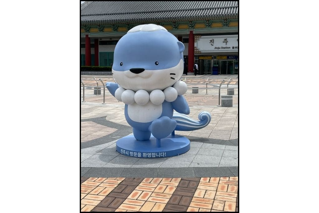Hamo, the sea otter mascot of Jinju, wears a pear necklace as he stands in front of the Jinju KTX station