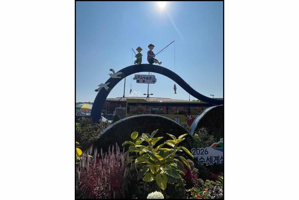 A flower garden with a sign with 2 figures fishing off the top, in Yeosu Korea