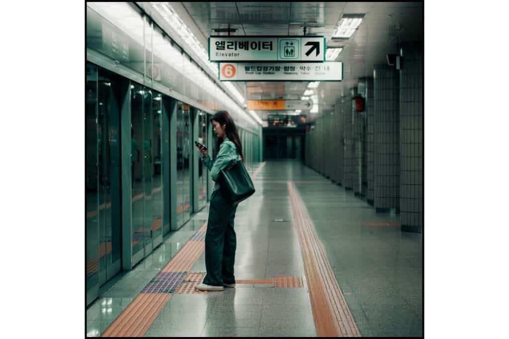 A woman looking at her phone while waiting for the subway alone in South Korea