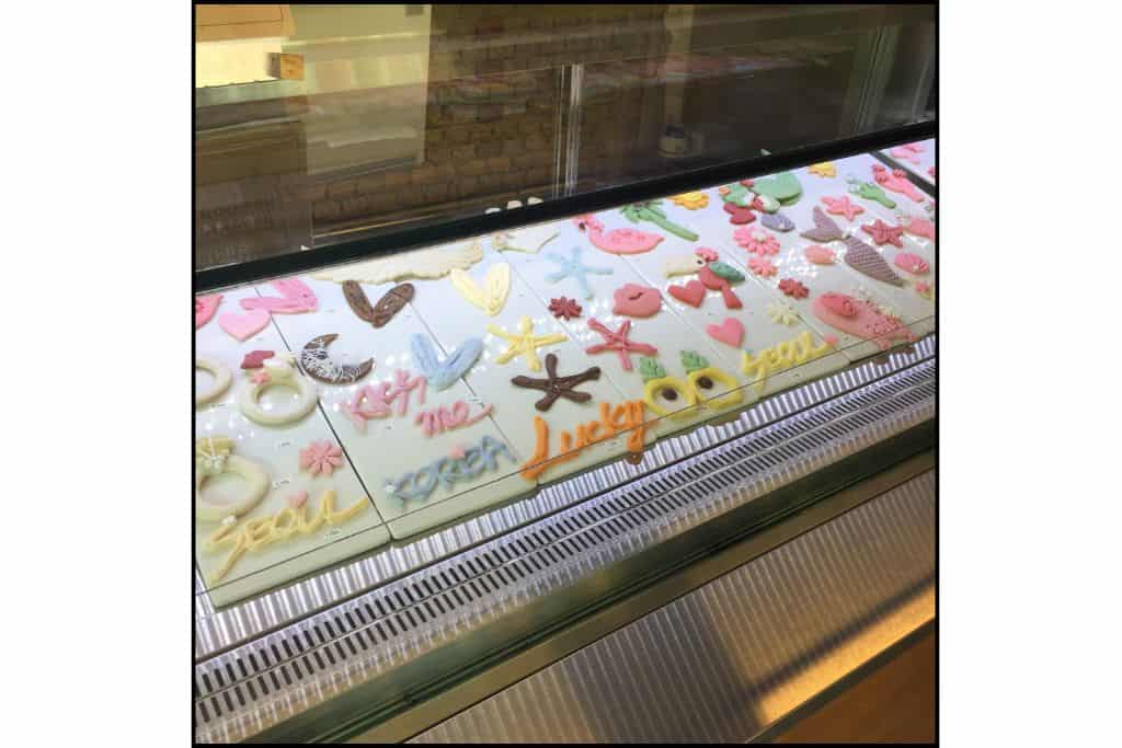 A display case at Biseu Topping showcasing an assortment of decorative cookies in various shapes, including stars, hearts, mermaid tails, and flowers, perfect for customizing ice cream cones.