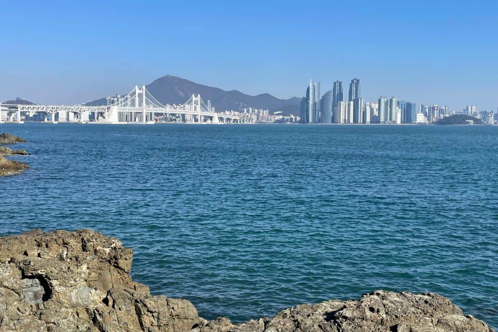 View of Gwangan Bridge stretching over the ocean with the iconic buildings at Haeundae Beach in the distance, Busan, South Korea.