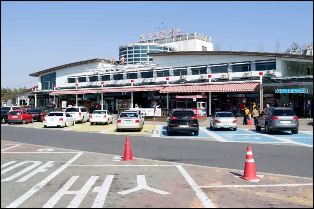 A busy Korean highway rest stop (hyugeso) with a variety of food stalls offering snacks like hotteok and hodu-gwaja, a convenience store, and clean restroom facilities.