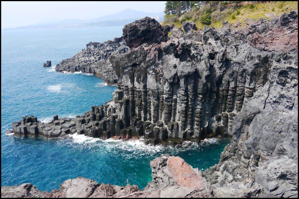 Columnar basalt rock formations at Jusangjeolli Cliffs along the turquoise coastline of Jeju Island, South Korea