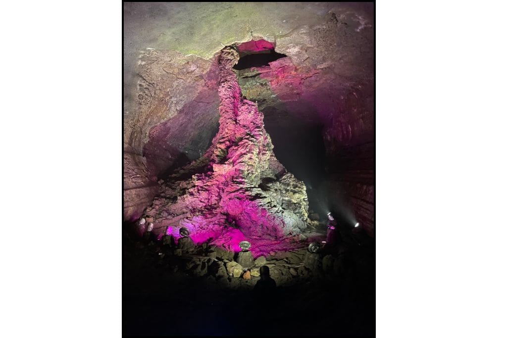 Illuminated lava column inside Manjanggul Lava Tube on Jeju Island, South Korea, with purple and pink lighting highlighting the rock formation