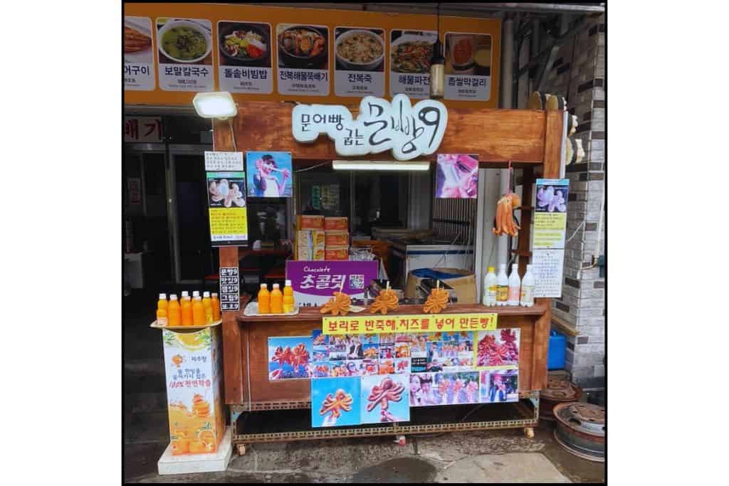 Street food stall on Jeju Island, South Korea, selling cheese-filled Munoppang — octopus-shaped pastries — alongside fresh tangerine juice and local treats.