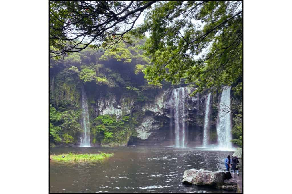 Cheonjeyeon Waterfalls cascading into a misty pool surrounded by lush greenery on Jeju Island, South Korea