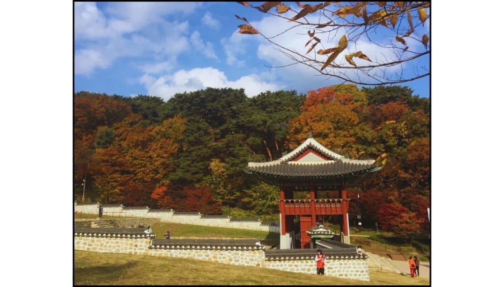 Traditional Korean pavilion at Namhansanseong Fortress surrounded by colorful autumn trees under a blue sky with puffy white clouds