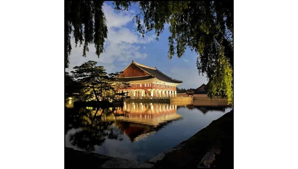 Night view of Gyeonghoeru Pavilion at Gyeongbokgung Palace in Seoul, South Korea, reflecting in the water with trees framing the scene