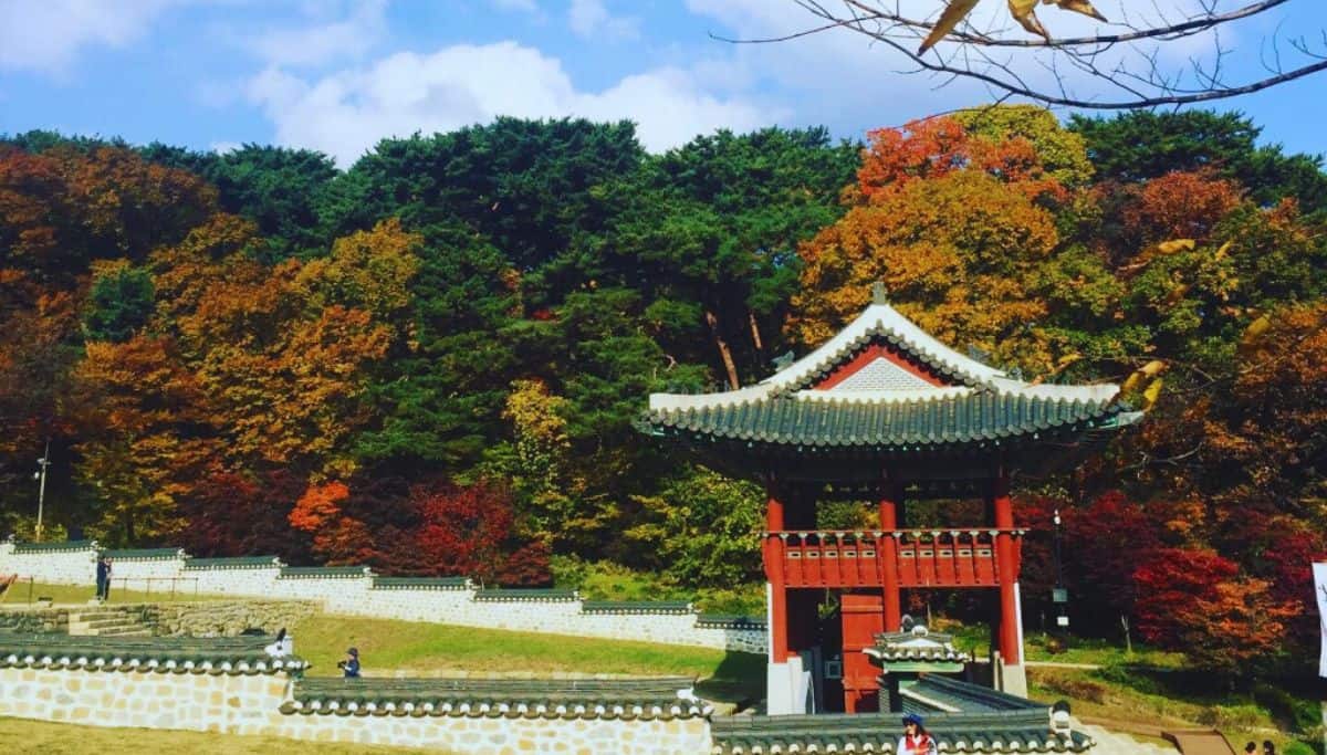 Autumn foliage at Namhansanseong Fortress near Seoul with a traditional red and green pavilion against colorful fall trees.