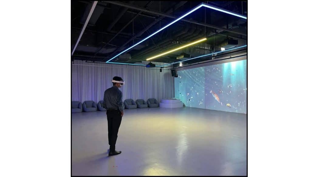 A visitor wearing a VR headset inside The CAVE VR Gallery in Seoul, with digital underwater projections on the wall.