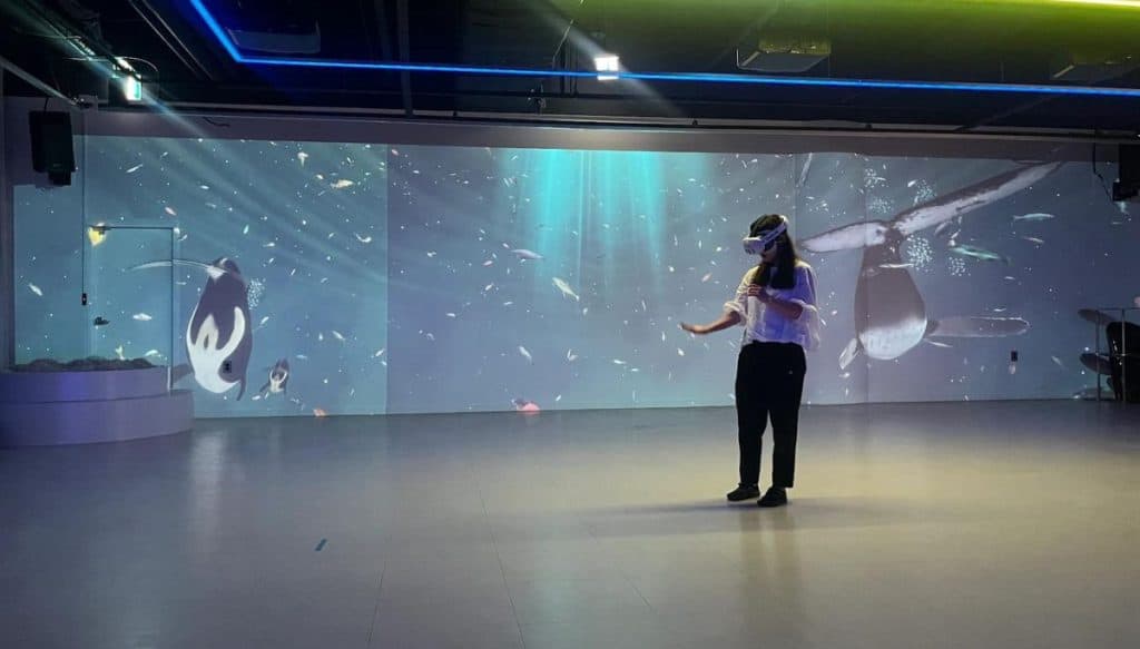 Person wearing a VR headset at The CAVE VR Gallery in Seoul, experiencing the Blue Walk exhibition with immersive whale and ocean projections