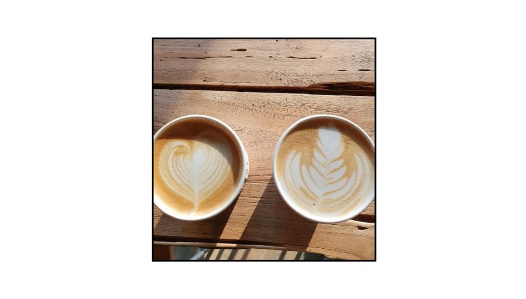 Two lattes with latte art on a wooden café table, photographed in warm natural light.