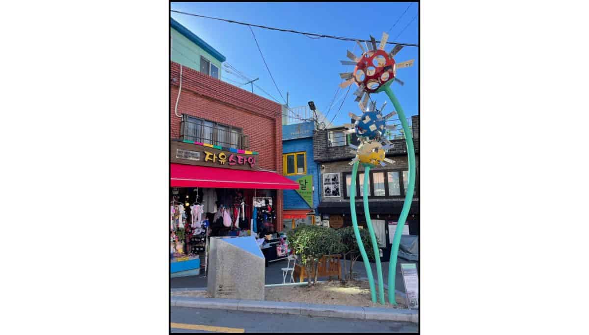 Colorful street scene at Gamcheon Culture Village in Busan with local shops and public art sculpture
