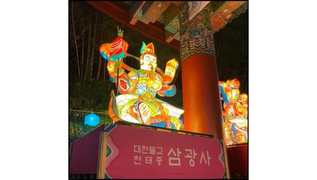 Illuminated lantern figures beneath the entrance gate at Samgwangsa Temple during the Buddha’s Birthday lantern festival at night.