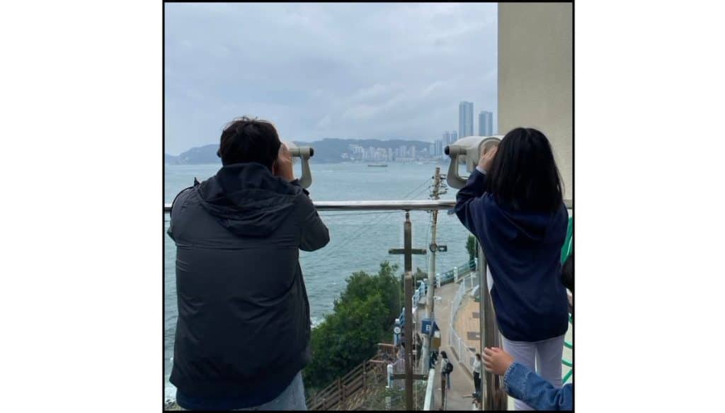 Visitors looking through public binoculars at the seaside viewpoint in Huinnyeoul Culture Village, Busan