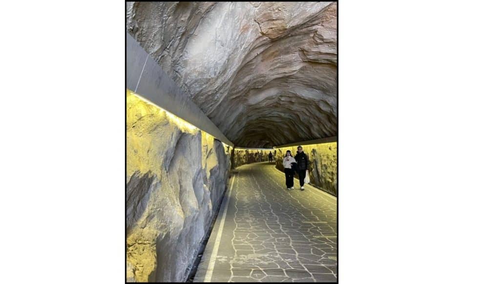 Inside view of the seaside tunnel at Huinnyeoul Culture Village showing textured rock walls and walkway with two people walking