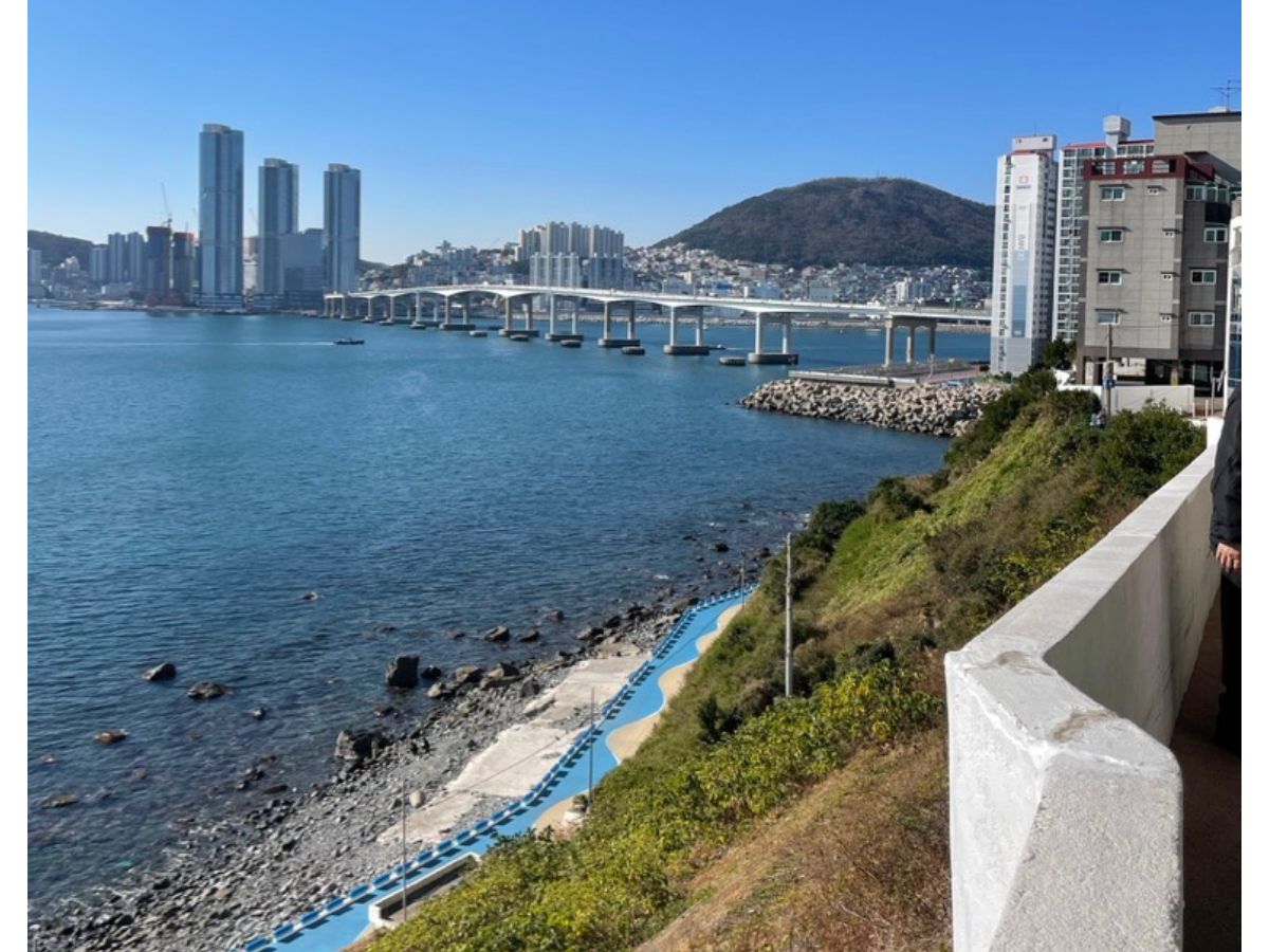 View from Huinnyeoul Culture Village overlooking the Busan coastline, blue seaside walkway, and bridge across the harbor