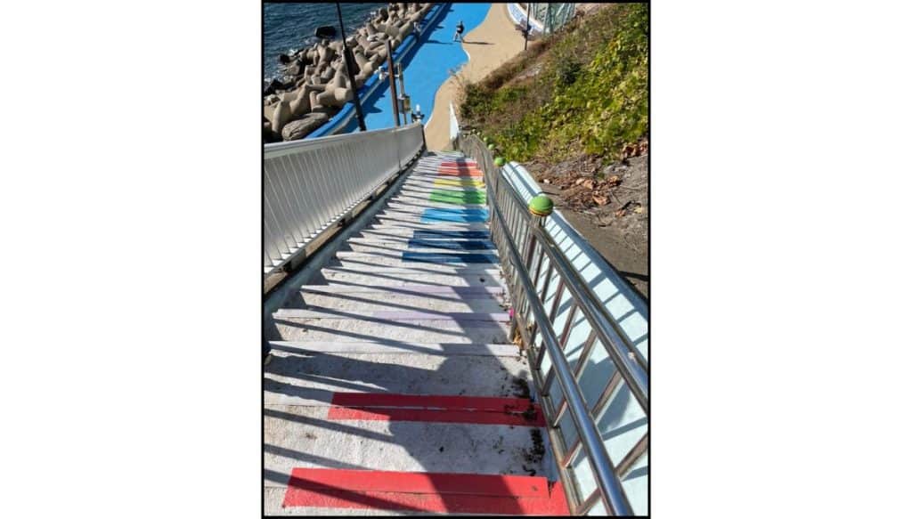 Staircase painted in bright colors like piano keys leading to the ocean walkway at Huinnyeoul Culture Village