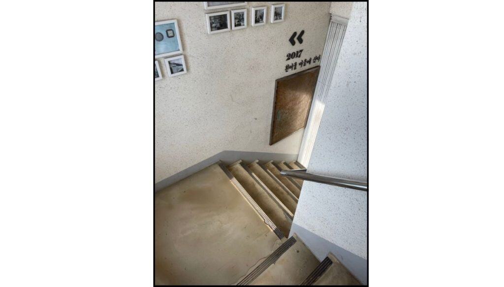 Staircase inside a Huinnyeoul Culture Village building with wall-mounted photos and handrail