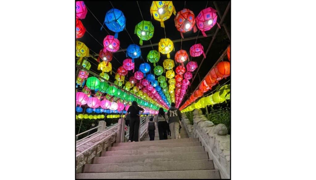 People walking up stone steps beneath rows of colorful lotus lanterns at Samgwangsa Temple during the Buddha’s Birthday lantern festival.