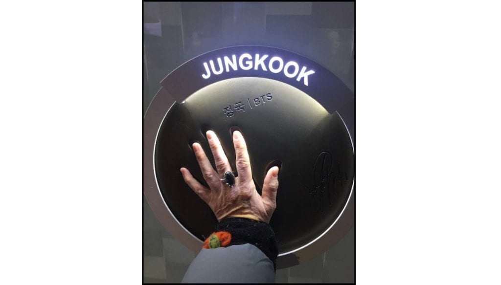 Hand touching Jungkook BTS handprint display plaque, with signature visible and ring on the hand.