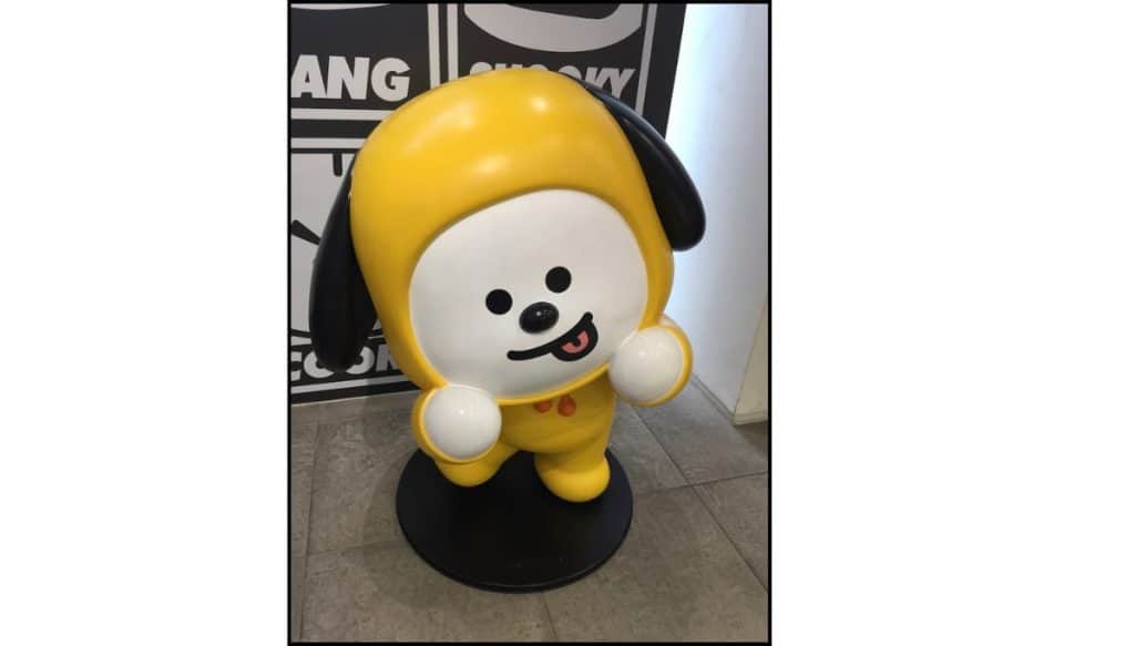 Large BT21 Chimmy character statue in a yellow outfit, smiling indoors on a display stand.