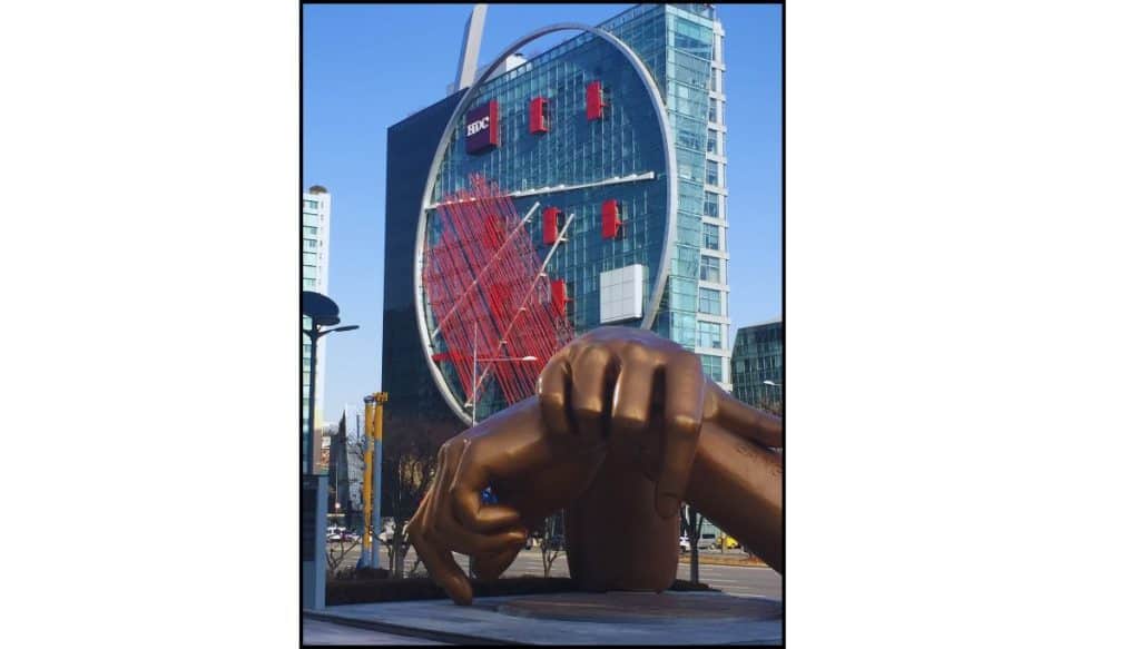 Large bronze hand sculpture in Gangnam with a modern glass building in the background.