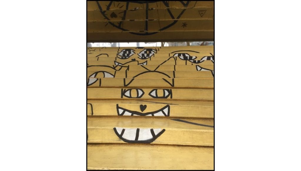 Staircase in Hongdae  painted yellow with playful black-and-white monster faces and cartoon eyes.