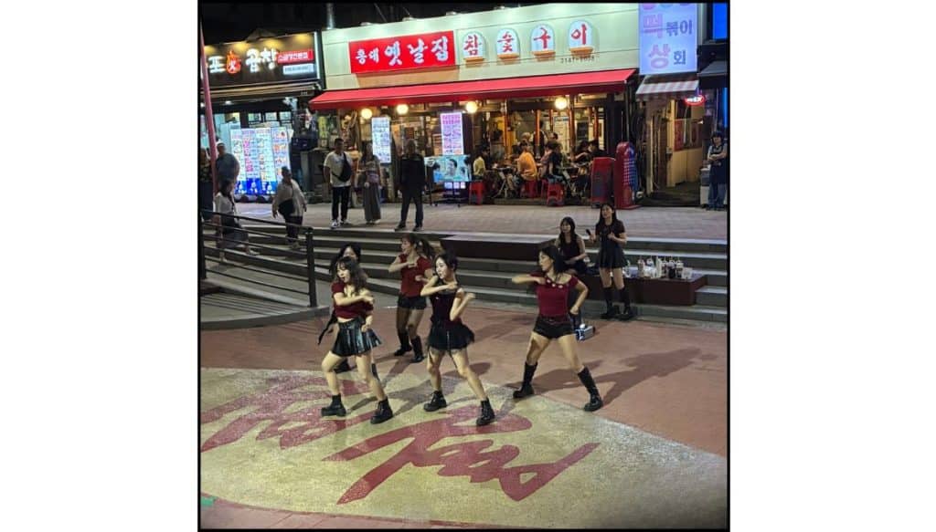 Large crowd gathered around a K-pop dance performance on a brightly lit pedestrian street in Hongdae, Seoul.