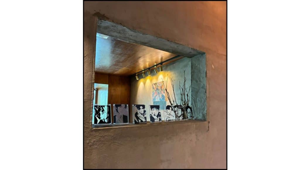 Large interior window at Hyuga Cafe in Gangnam, Seoul, looking into a warmly lit room with BTS photos and memorabilia lined along the ledge