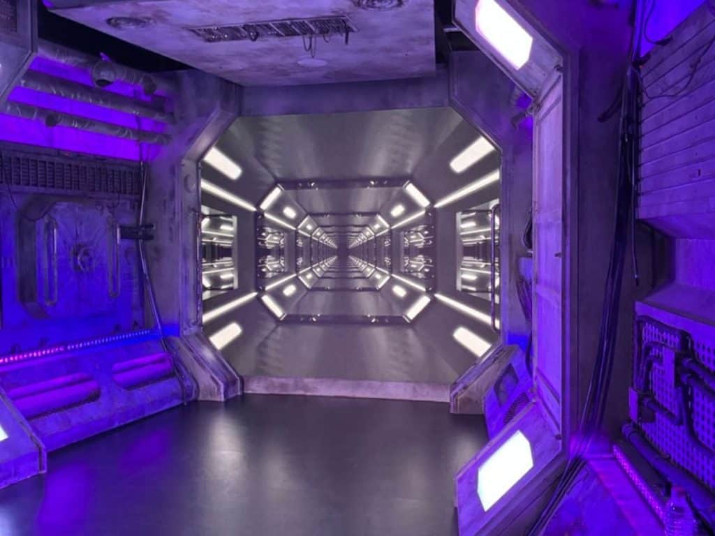 A futuristic tunnel-style photo zone with purple lighting, metallic walls, and a bright walkway that looks like the inside of a spaceship.