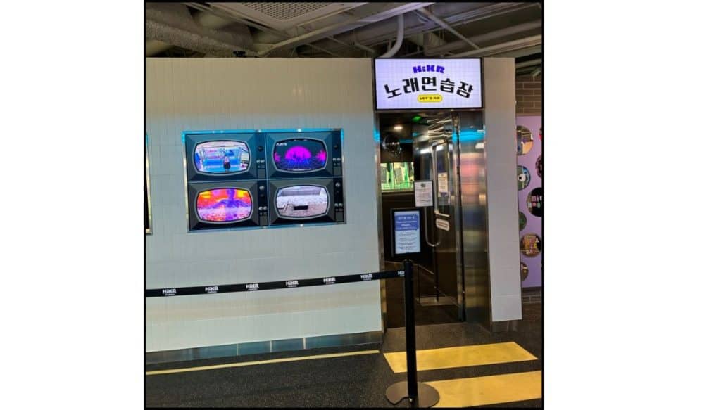 Karaoke practice room entrance with colorful screen displays and a Korean sign inside HiKR Ground.