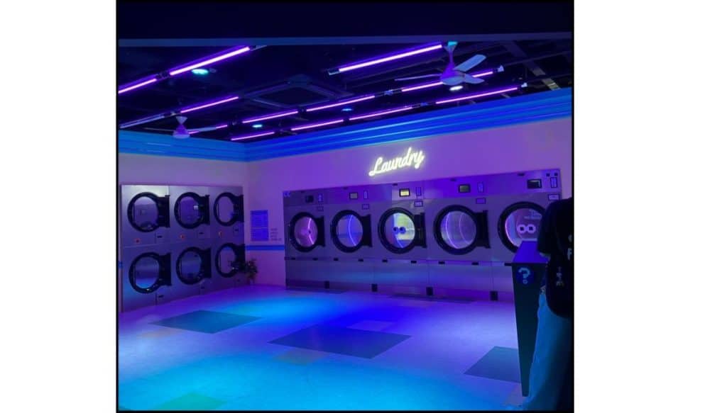 Purple-lit laundromat-style set with washing machines lined against the wall inside HiKR Ground.