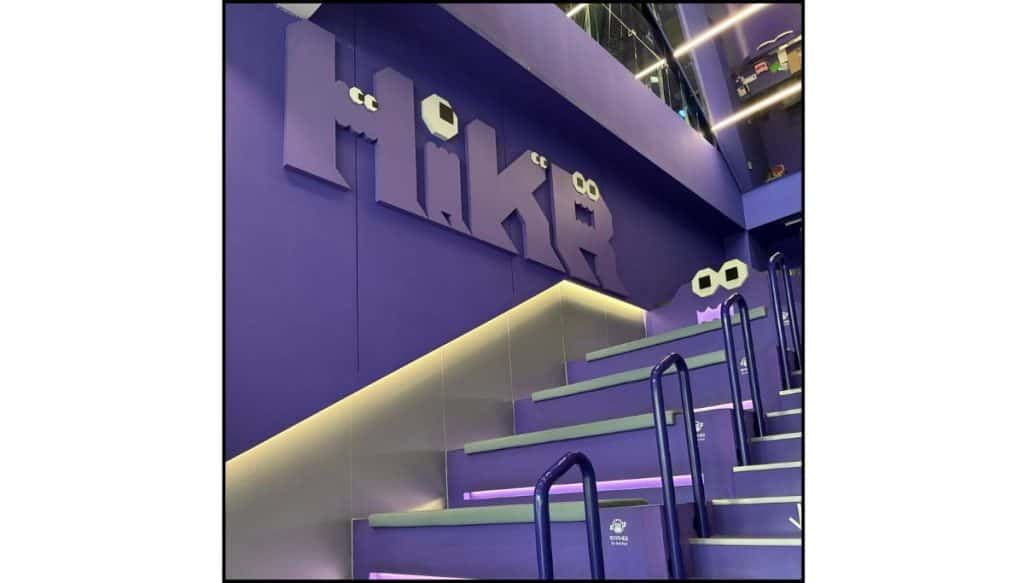 A purple-lit indoor seating area with tiered steps, glowing lights, and a futuristic stage-like feel.