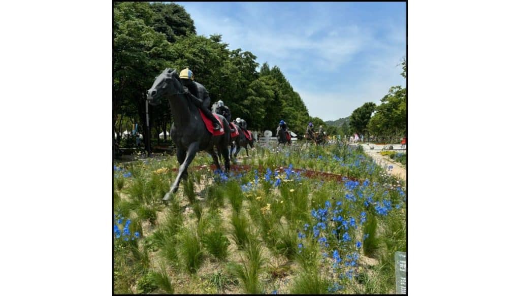 Horse sculptures surrounded by blue flowers and greenery at Seoul Forest during a sunny spring day.