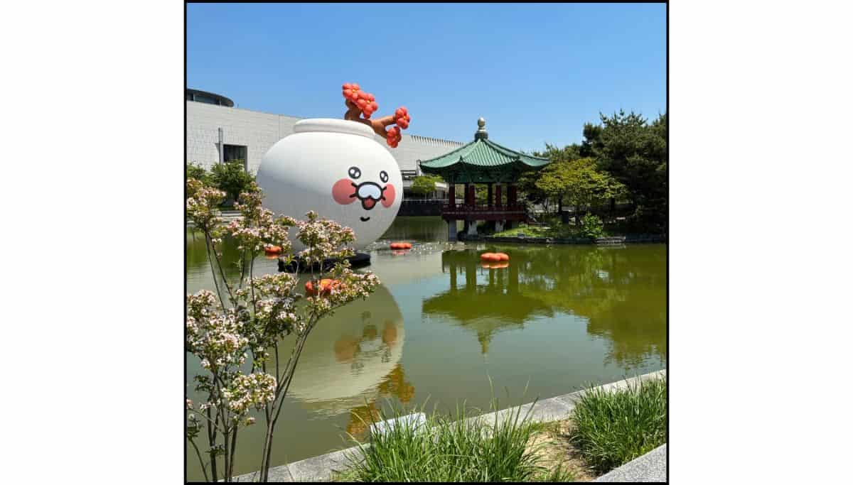 Large white character display floating in a pond beside a traditional Korean pavilion at the National Museum of Korea.