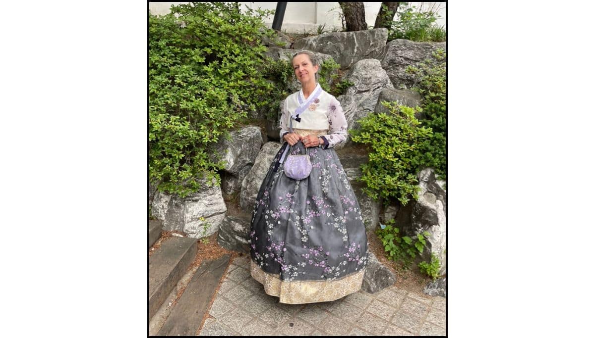 AWoman wearing a graytraditional Korean hanbok, standing in front of some rocks and bushes during a Seoul itinerary stop in South Korea.
