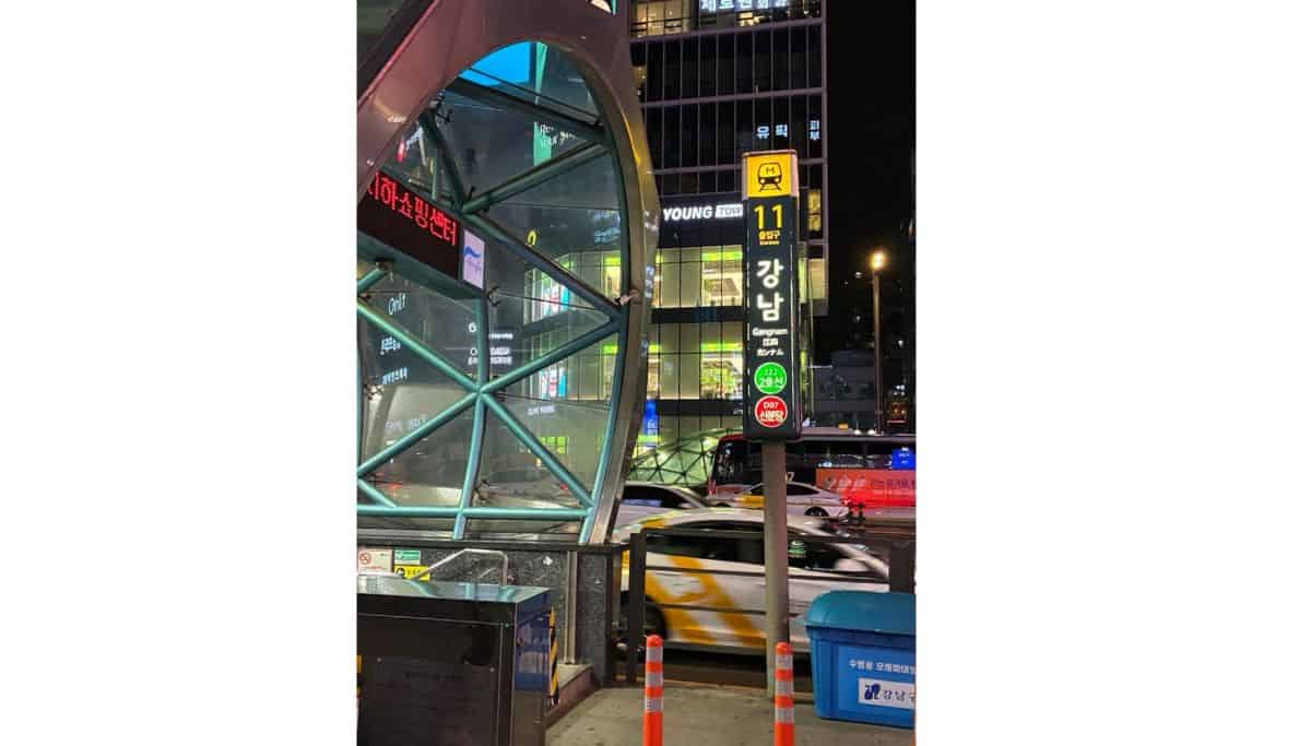 Gangnam Station Exit 11 in Seoul at night, with the subway entrance, street signs, and traffic in the background.