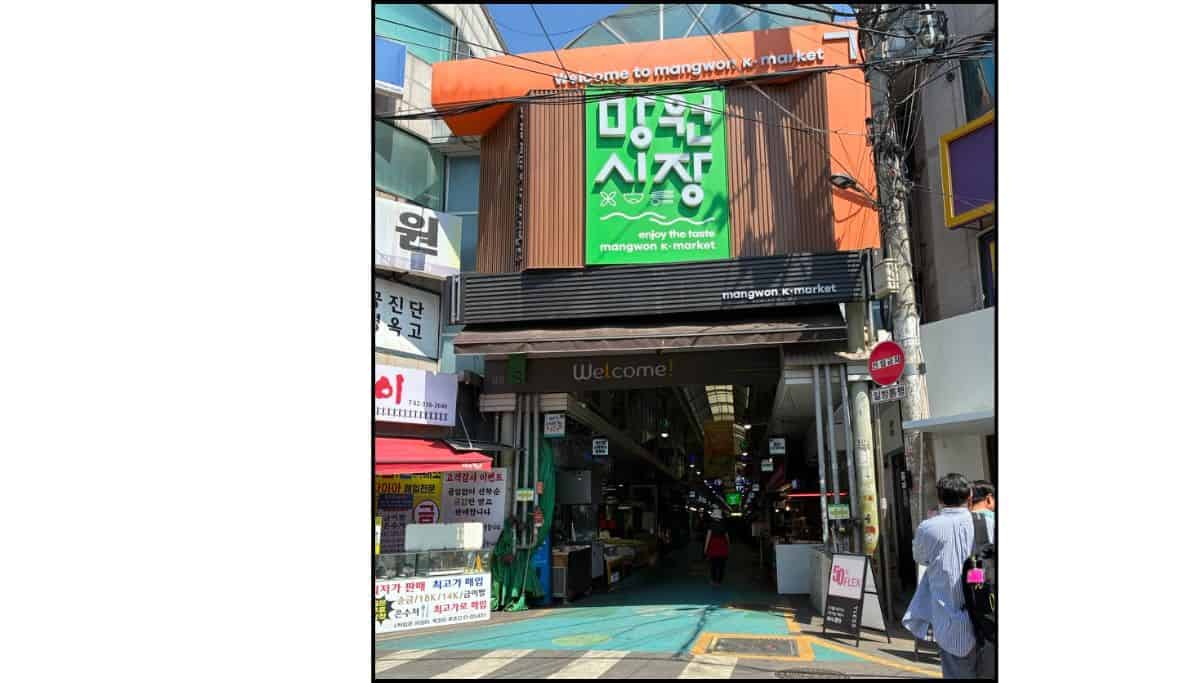 Entrance to Mangwon Market, a traditional market in Seoul, with its orange and green sign above the covered shopping arcade.